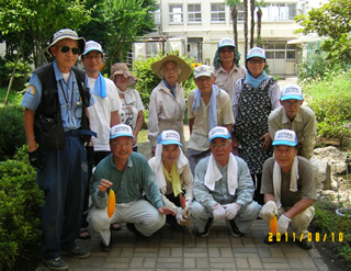 中野区環境井戸端会議のメンバーと地域の皆さん。鈴木さんは、前列左端で黄色く熟したゴーヤをぶら下げている。
