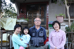 校長の浅原俊宏さん（中央）、奥さんのゆかりさん（右）、事務局の宿谷珠美さんと愛娘のあいかちゃん（左）。『自然の学校』の看板を掲げた浅原家の自宅前にて。