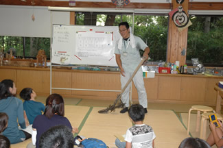 田の草取りに使う「田掻車（たかきぐるま）」を手にする博物館学芸員の佐藤智敬さん。今日の農作業の内容と、作業に関連したお話をしてくださった。